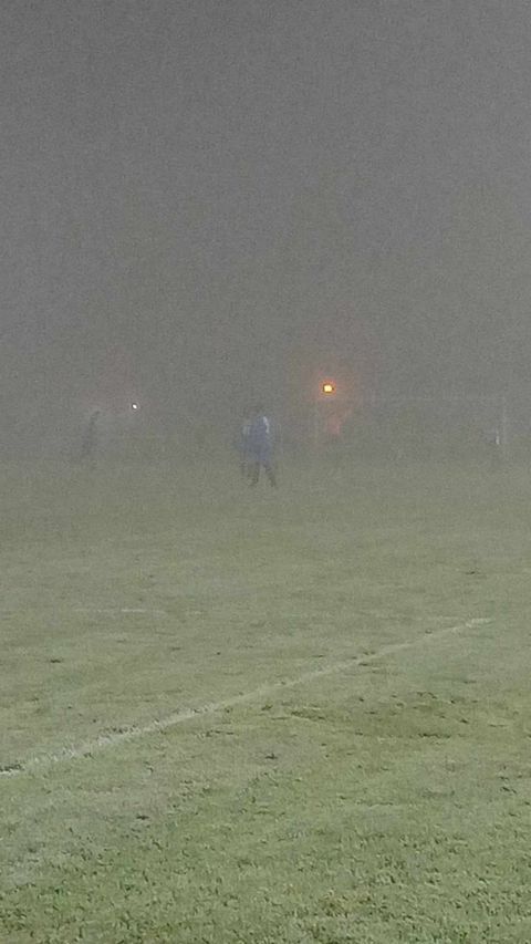 Un groupe de personnes joue au football dans le brouillard sur un terrain.