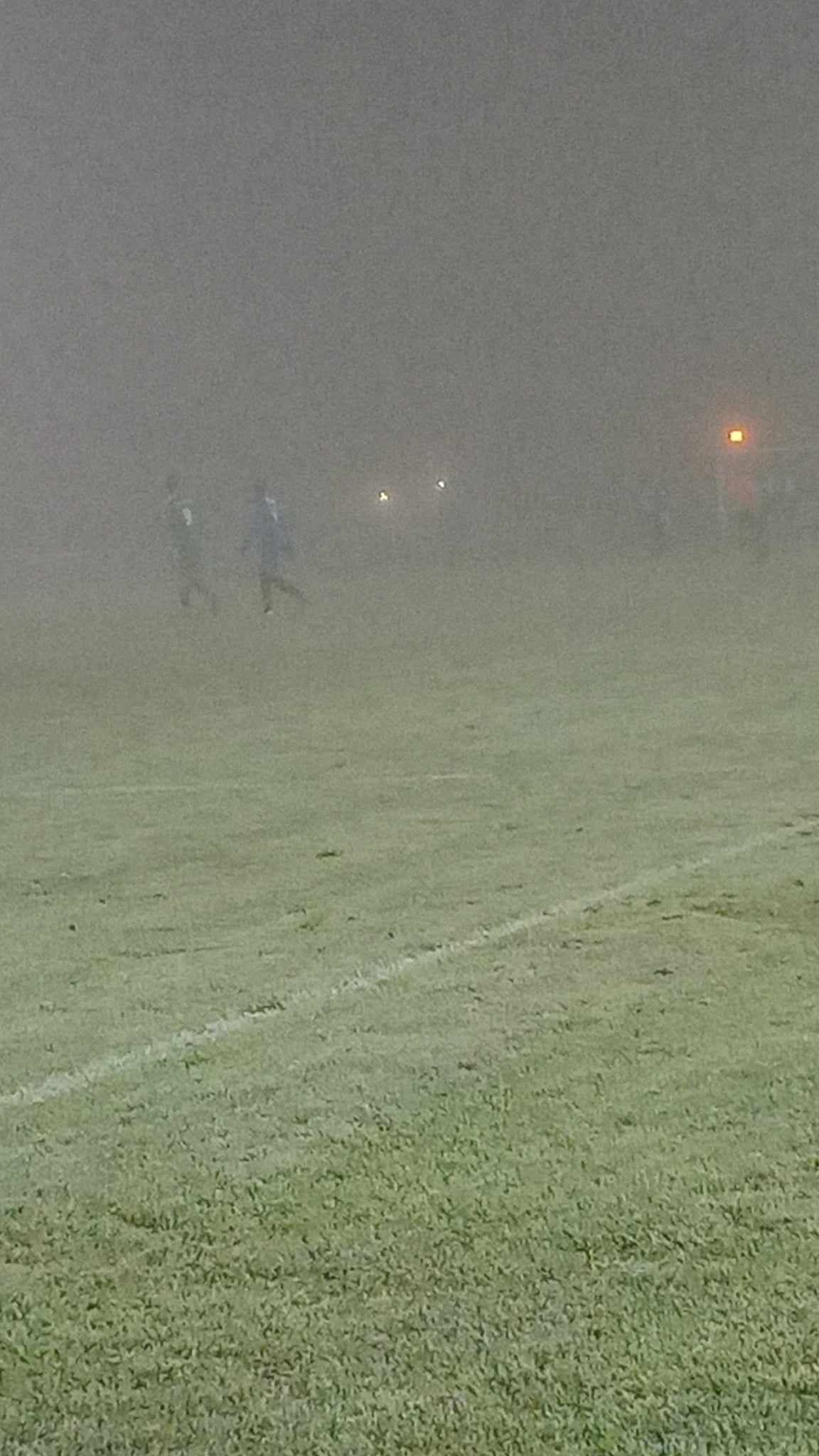 Un groupe de personnes joue au football dans le brouillard sur un terrain.