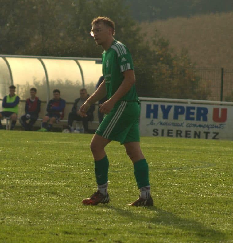 Un joueur de football se tient devant un panneau indiquant hyper u