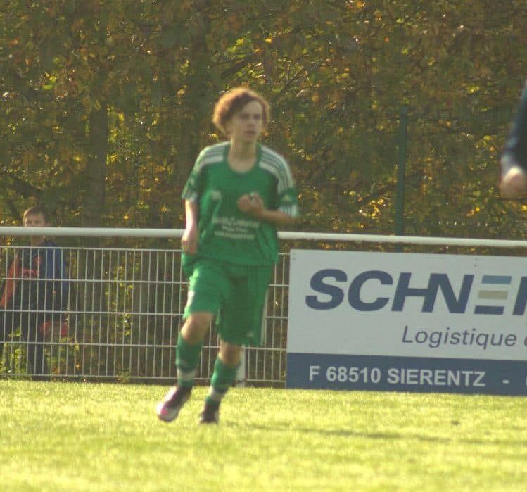 Un joueur de football court sur un terrain devant un panneau indiquant schnei