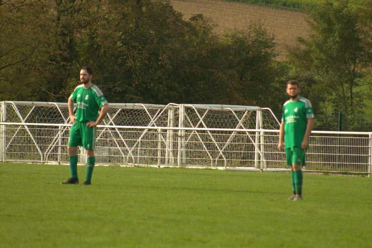 Deux hommes en uniformes de football verts se tiennent sur un terrain.
