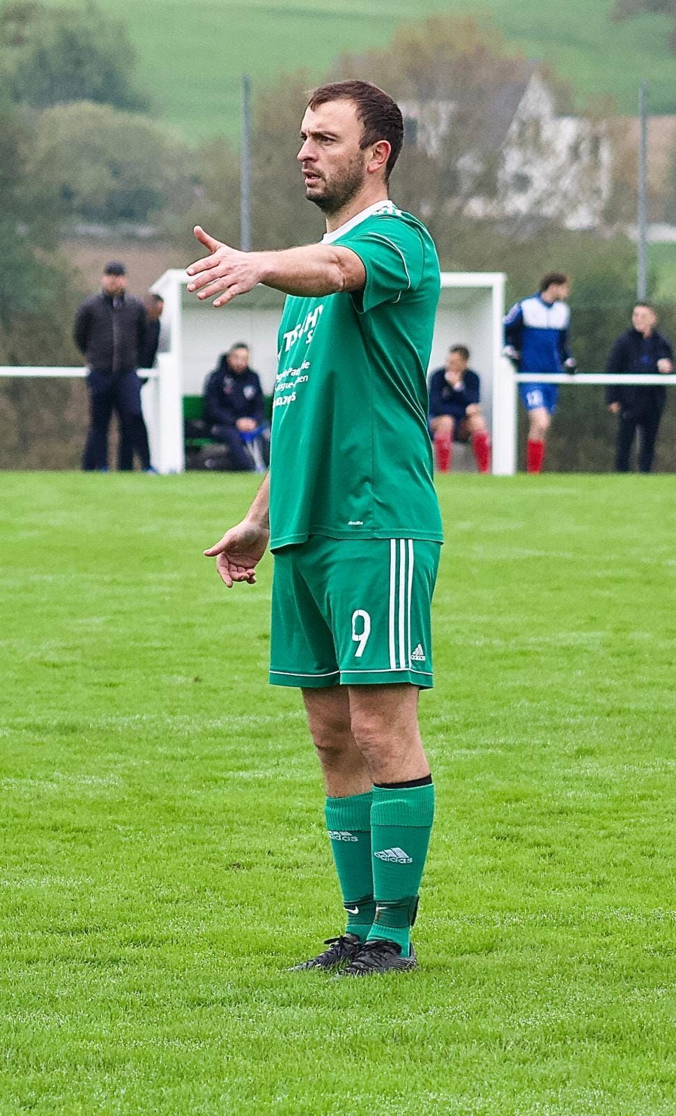Un homme en uniforme de football vert se tient debout sur un terrain.