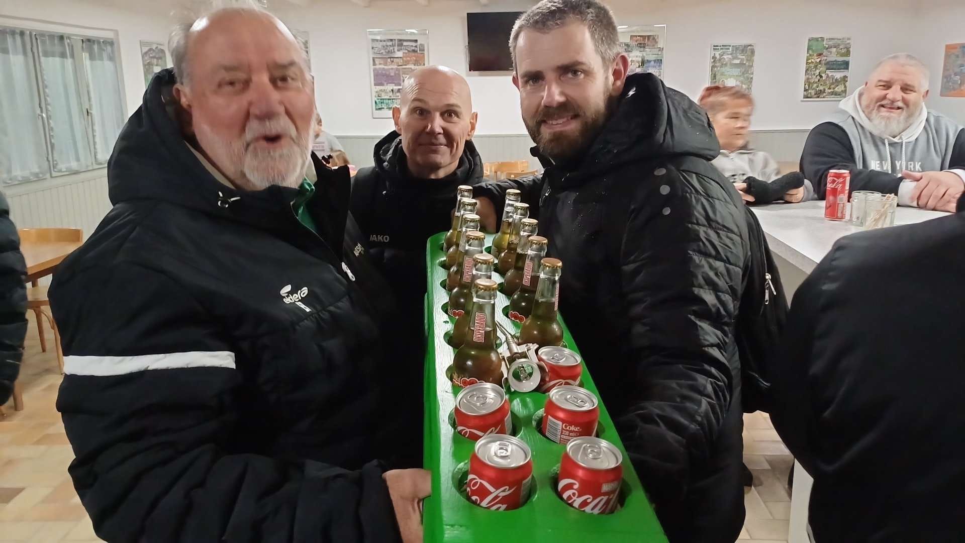 Un groupe d'hommes se tient debout autour d'une table tenant un plateau vert avec des canettes de Coca Cola dessus.