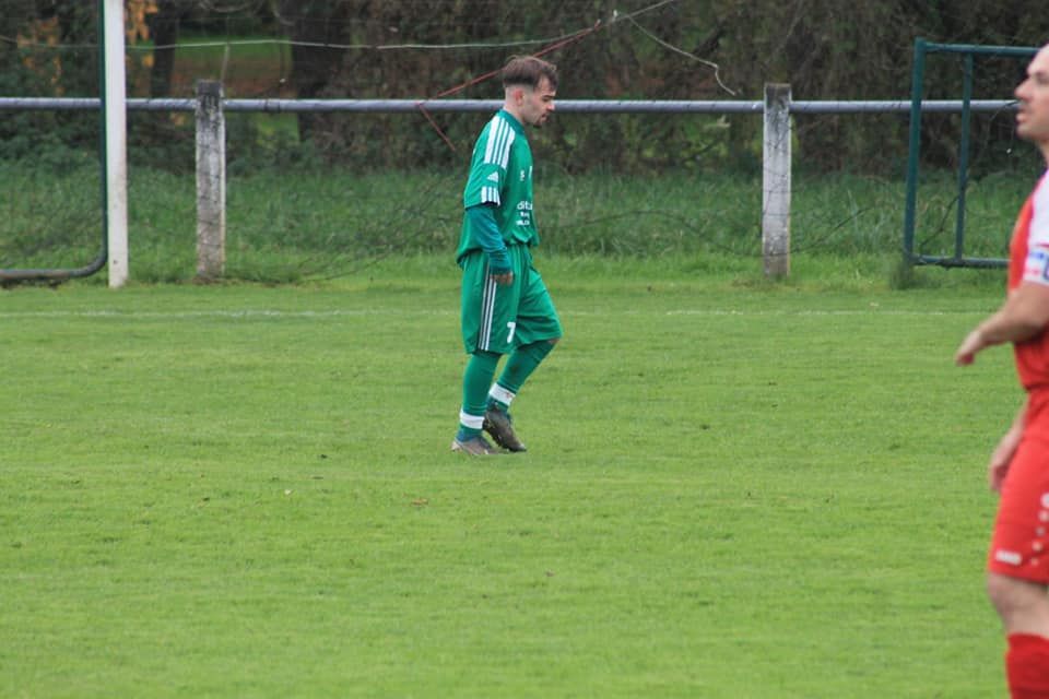 Un homme en maillot vert marche sur un terrain de football.