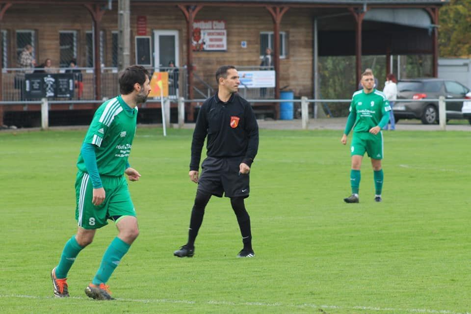 Un arbitre se tient sur un terrain de football et parle à deux joueurs de football.