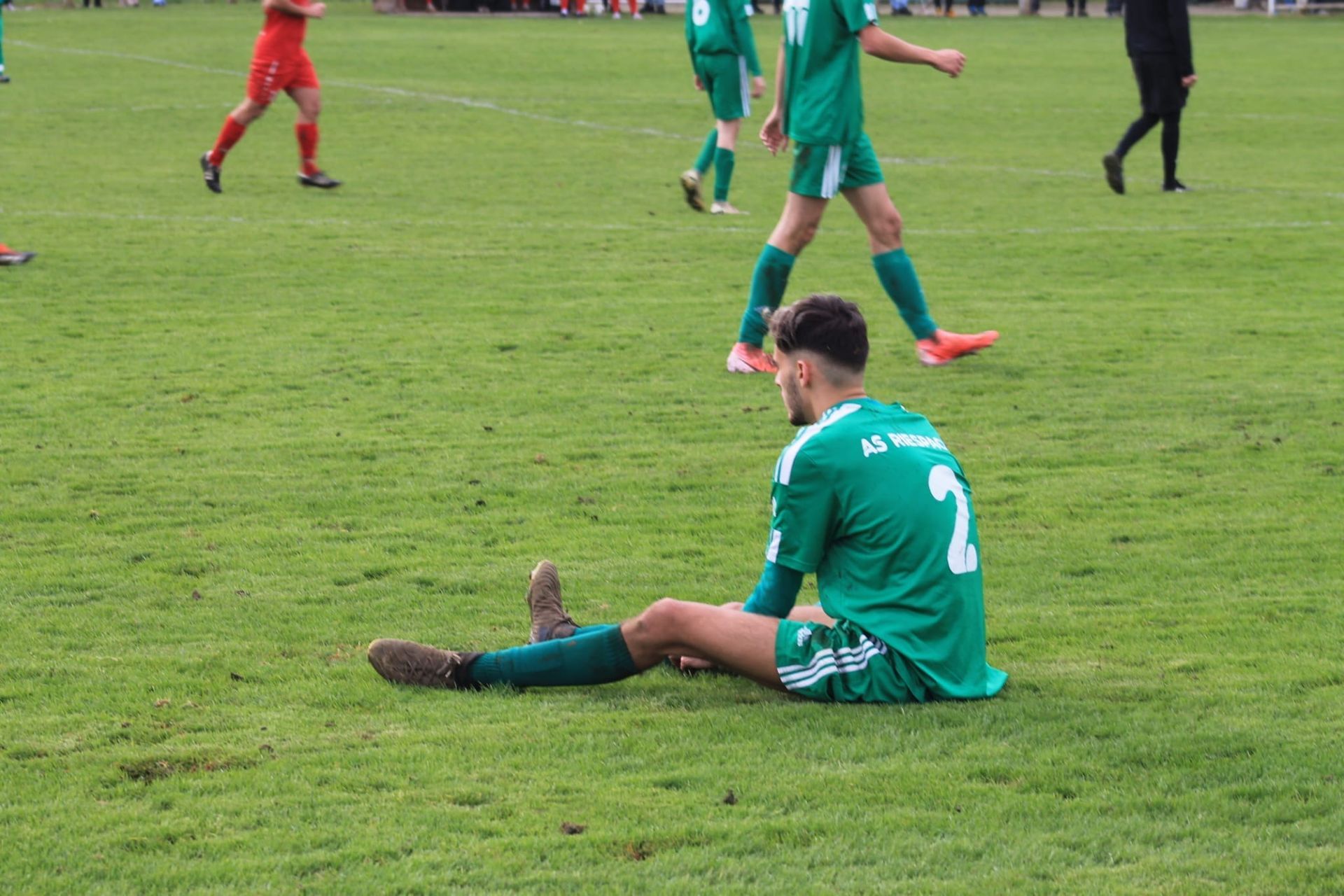 Un joueur de football est assis sur l'herbe pendant un match.