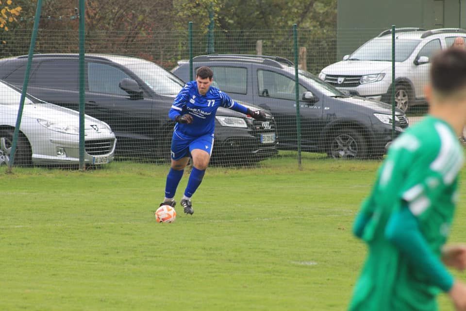Un homme en maillot bleu frappe un ballon de football sur un terrain.
