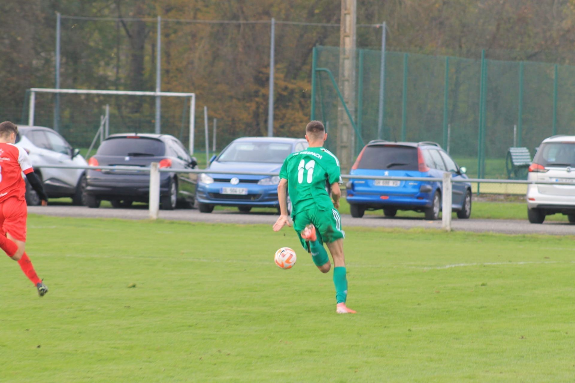 Un homme en maillot vert court avec un ballon de football sur un terrain.