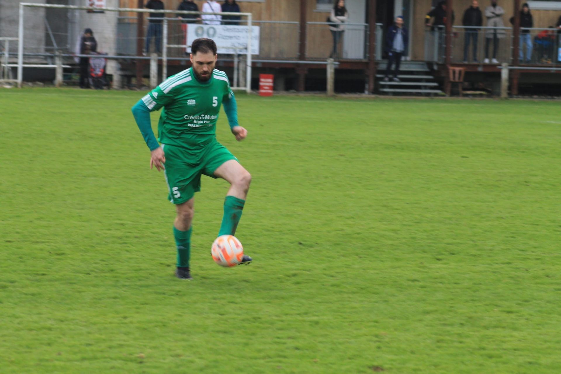 Un homme en maillot vert frappe un ballon de football sur un terrain.