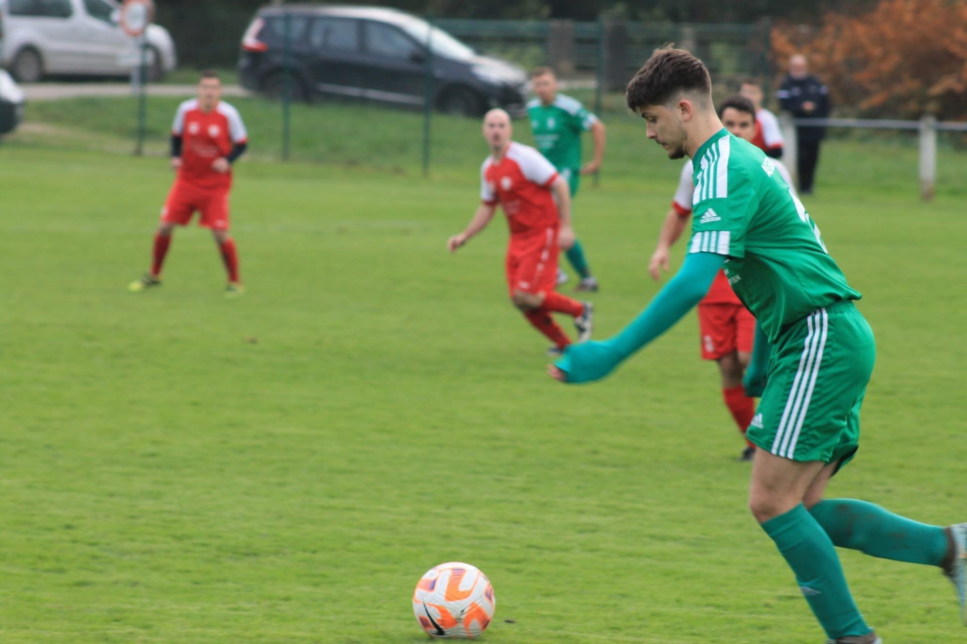 Un homme en maillot vert frappe un ballon de football sur un terrain.