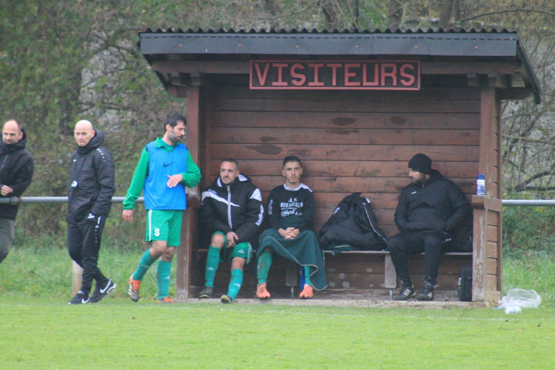 Un groupe d'hommes sont assis dans un abri en bois sur un terrain de football.