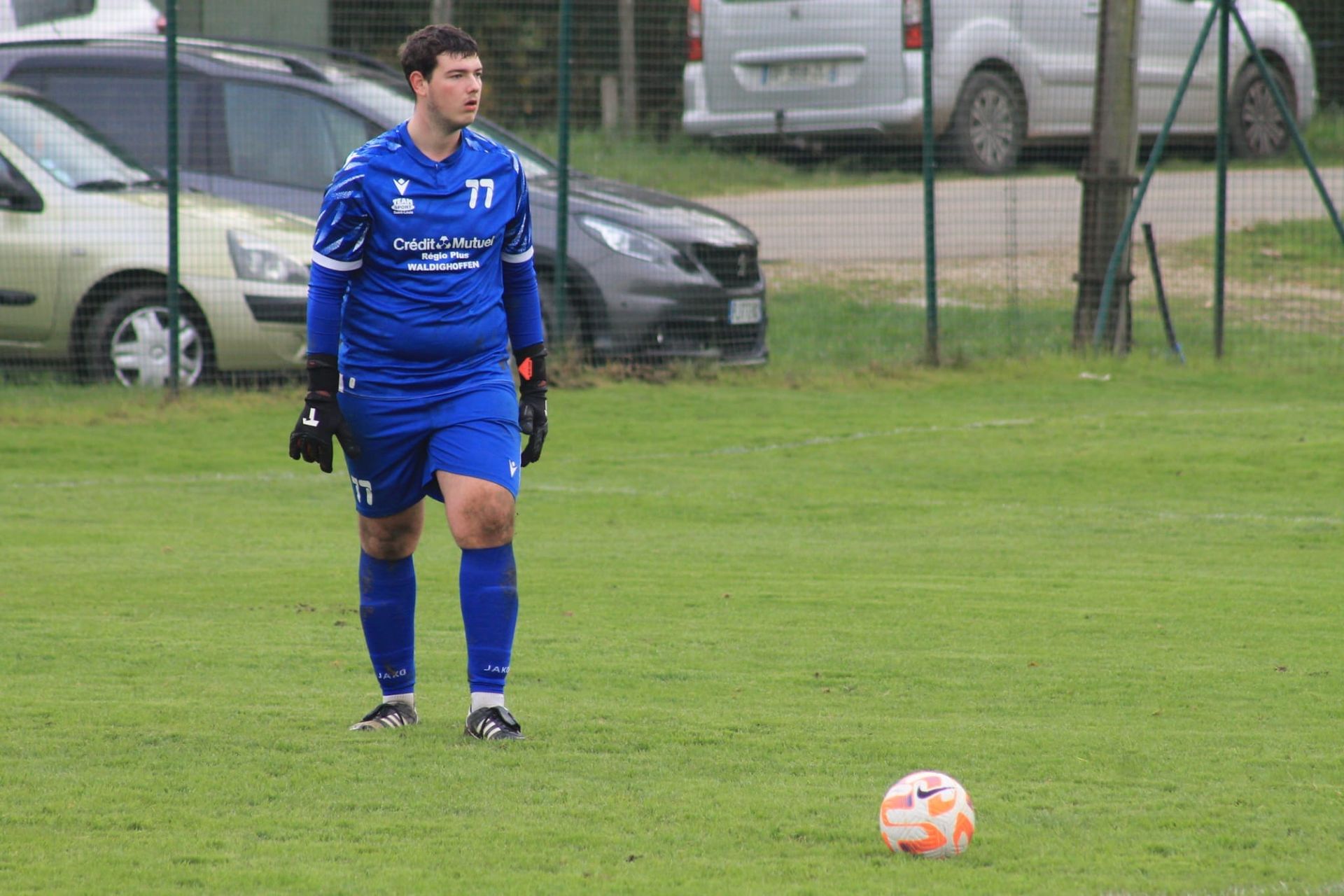 Un joueur de football se tient à côté d'un ballon de football sur un terrain.
