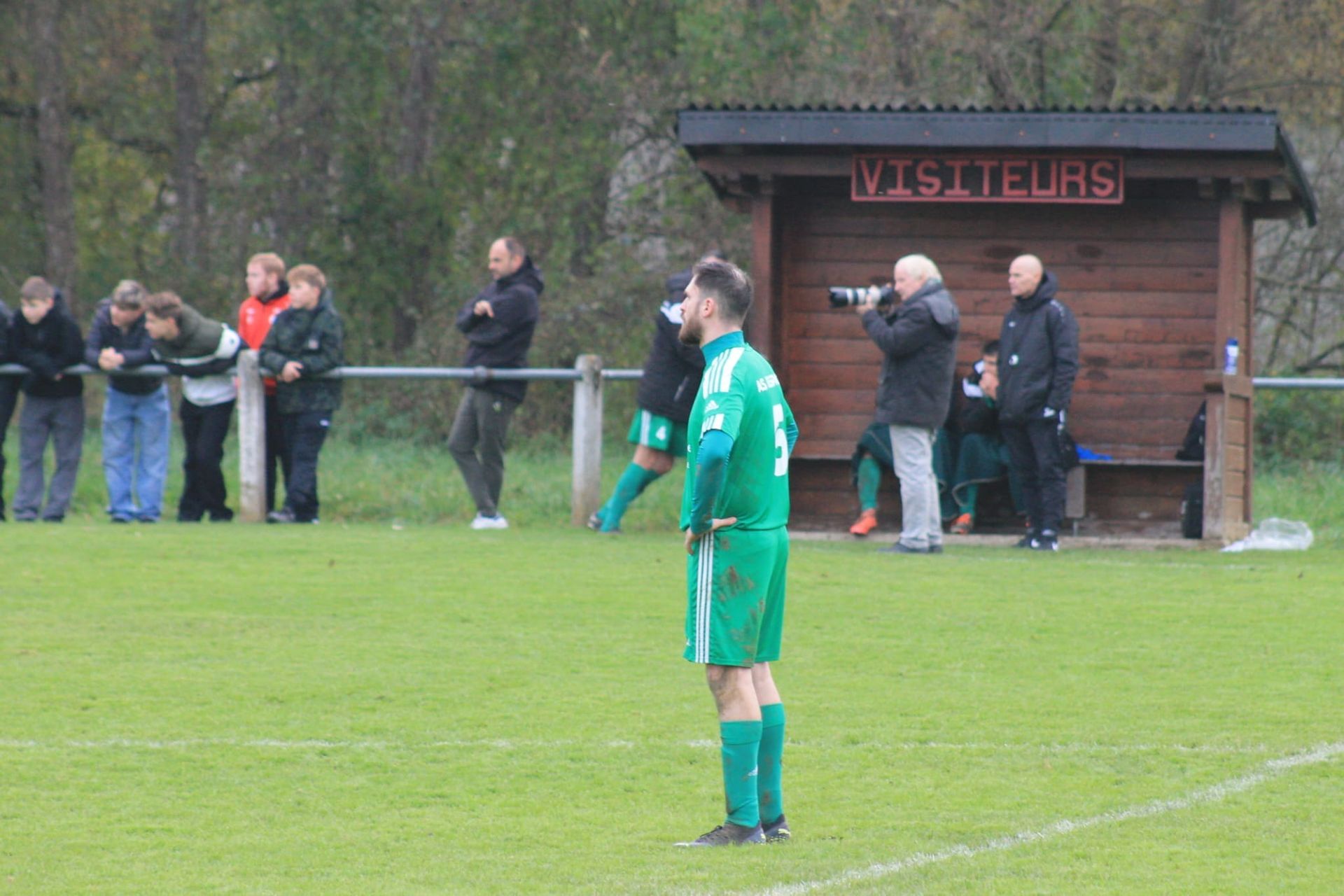 Un homme en maillot vert se tient debout sur un terrain de football.