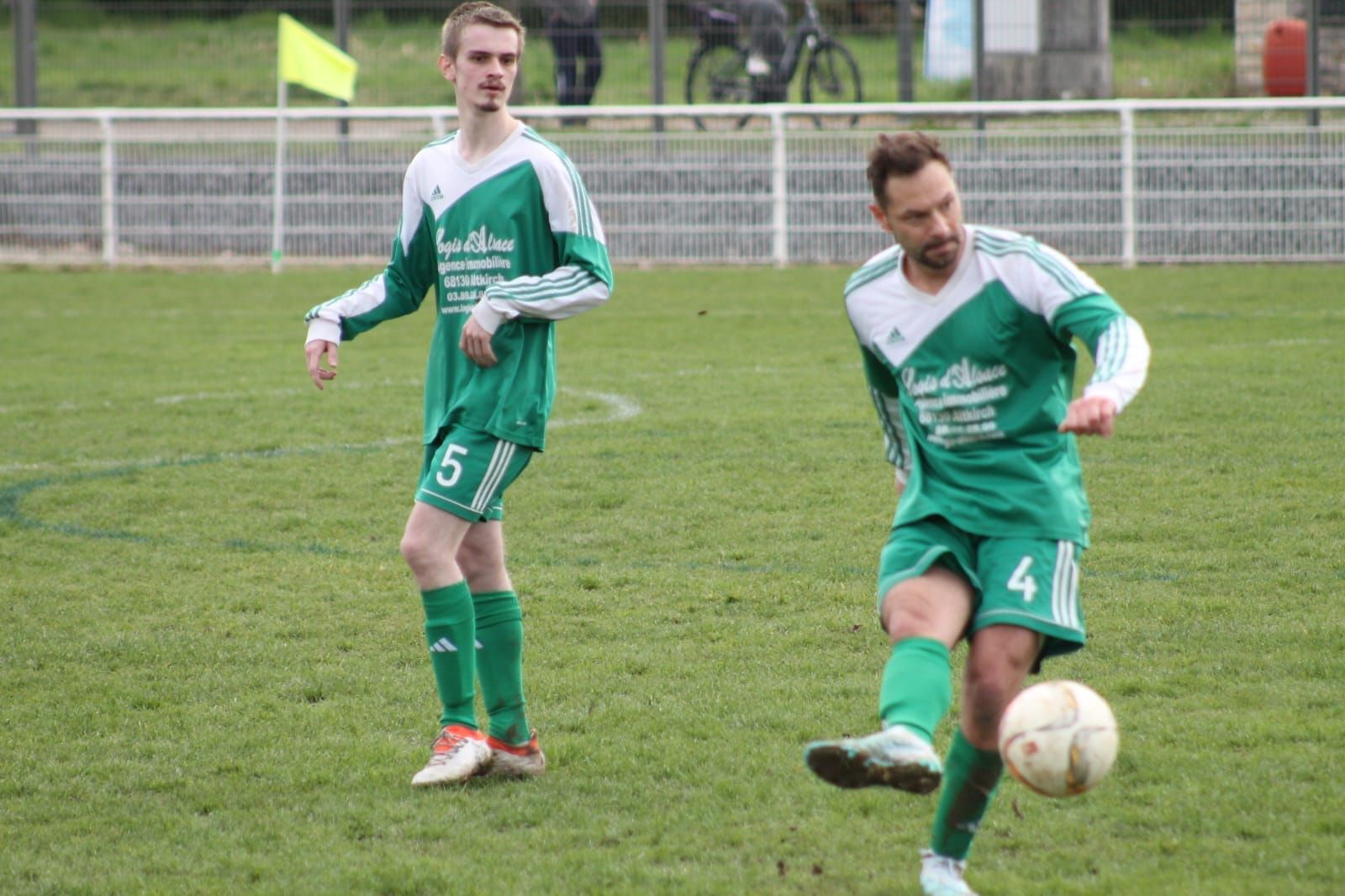 Un homme en uniforme de football vert se tient debout sur un terrain.