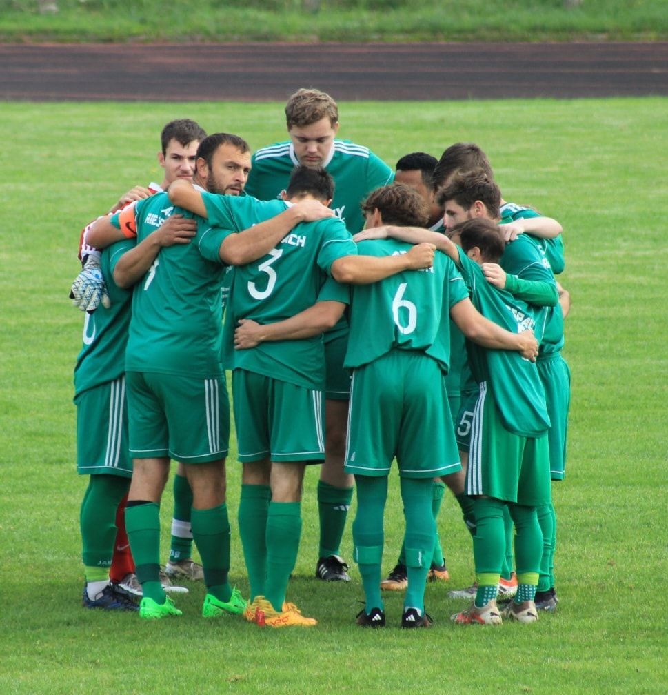 Un homme en uniforme de football vert se tient debout sur un terrain.