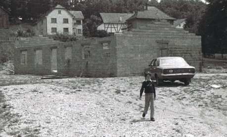 Une photo en noir et blanc d'un homme marchant devant une voiture.