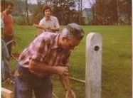 Un homme se tient à côté d'un poteau de clôture dans un champ.