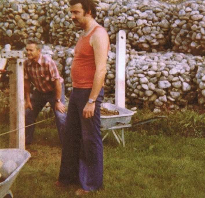 Un homme en débardeur rouge se tient à côté d'une brouette