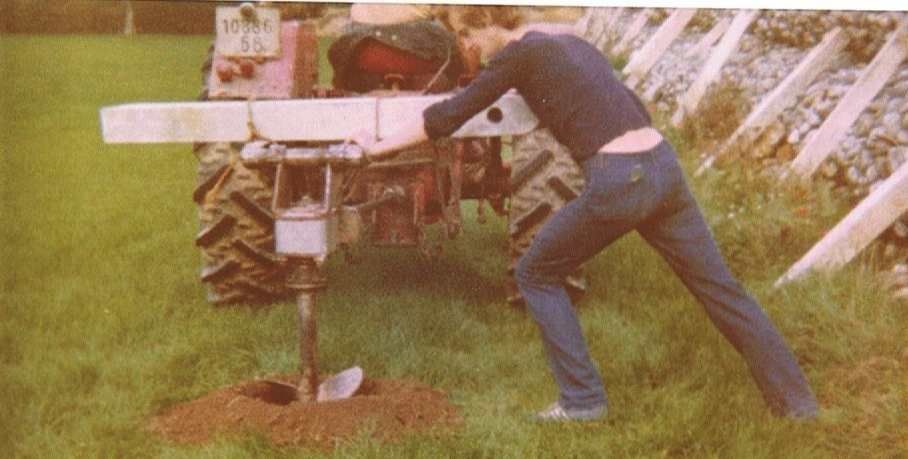 Un homme creuse un trou dans le sol devant un tracteur.