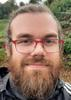 Un homme avec une barbe et des lunettes prend un selfie.