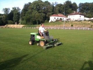 Un homme conduit une tondeuse à gazon sur un champ vert luxuriant.