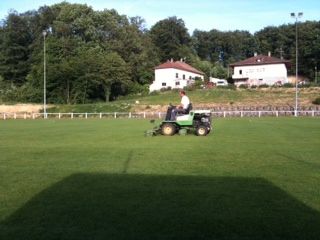 Un homme conduit une tondeuse à gazon sur un champ vert luxuriant