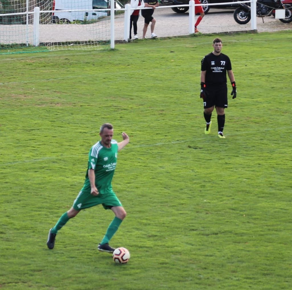 Un homme en chemise verte frappe un ballon de football