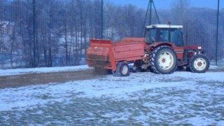 Un tracteur rouge tire une remorque dans la neige.