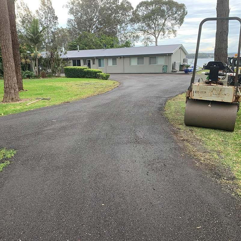 A Roller Is Sitting On The Side Of A Road In Front Of A House — Atholyn Earthmovers in Wyee, NSW