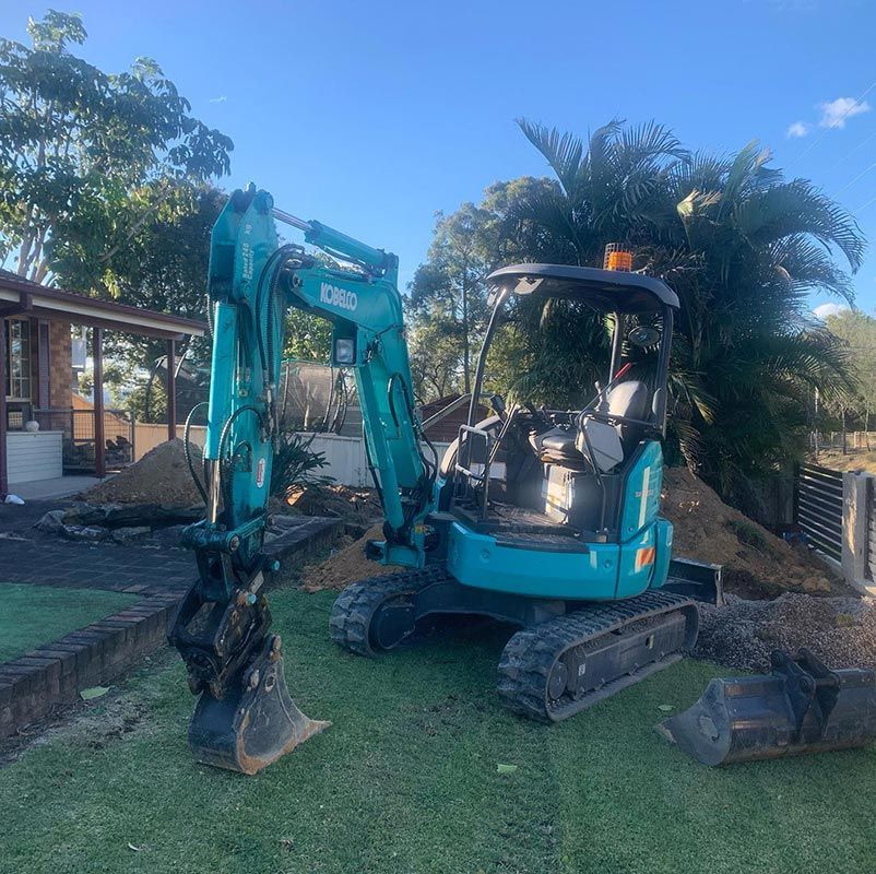 A Small Excavator Is Parked In The Grass In Front Of A House — Atholyn Earthmovers in Wyee, NSW