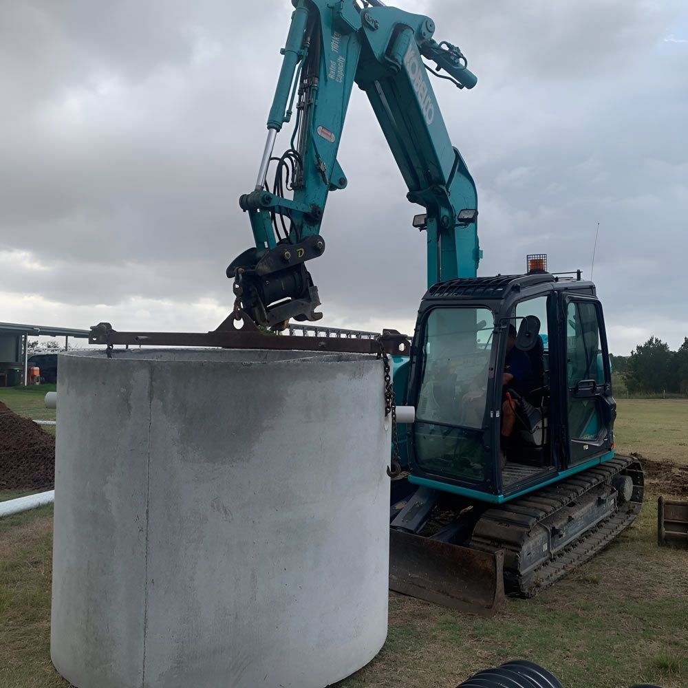 A Green Excavator Is Lifting A Large Concrete Septic Tank — Atholyn Earthmovers in Wyee, NSW