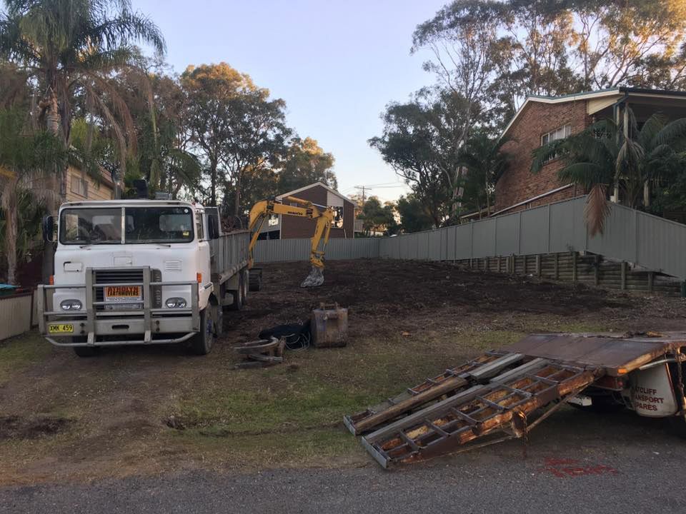 A White Truck With A Yellow Excavator On The Back Is Parked In A Yard — Atholyn Earthmovers in Maitland, NSW