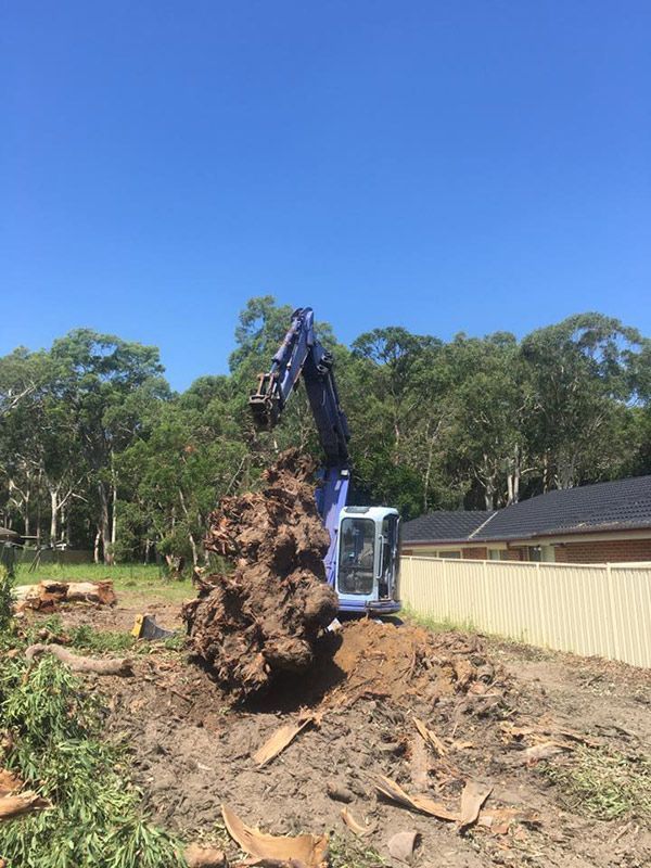 A Blue Excavator Is Moving A Large Pile Of Dirt In A Field — Atholyn Earthmovers in Wyee, NSW