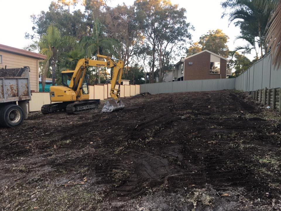 A Yellow Excavator Is Clearing The Backyard With Dump Truck — Atholyn Earthmovers in Maitland, NSW