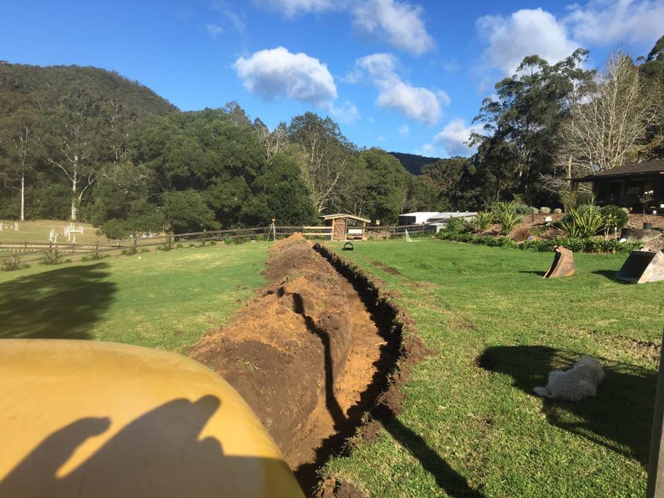 A Tractor Is Digging A Hole In A Grassy Field — Atholyn Earthmovers in Singleton, NSW