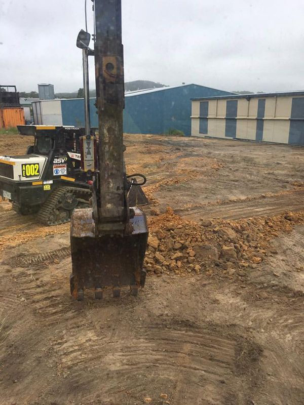 A Bulldozer Is Digging A Hole In The Dirt In Front Of A Building — Atholyn Earthmovers in Cessnock, NSW