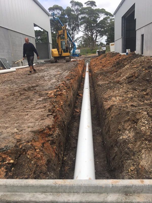 A Man Is Standing In A Trench Next To A Large Pipe — Atholyn Earthmovers in Wyong, NSW