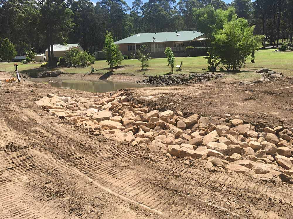 A Large Pile Of Rocks Is In The Middle Of A Dirt Field In Front Of A House — Atholyn Earthmovers in Gosford, NSW