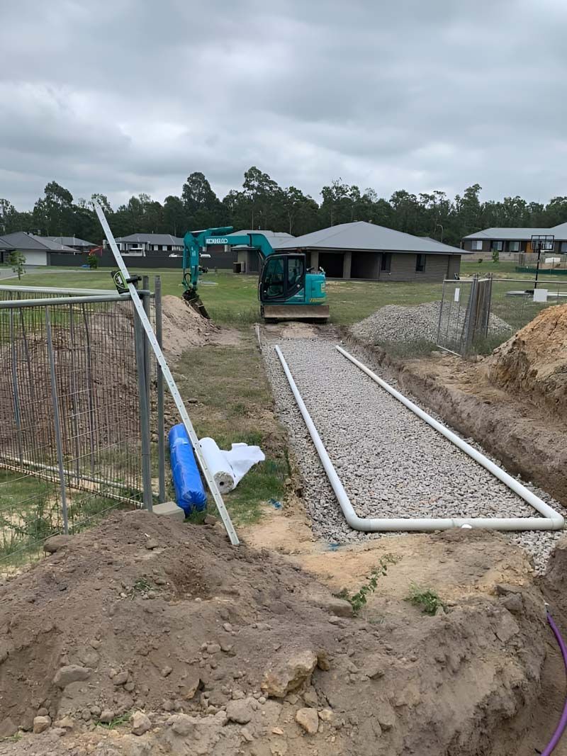 A Drainage System Is Being Installed In A Yard Next To A House With Kobelco Excavator — Atholyn Earthmovers in Wyee, NSW