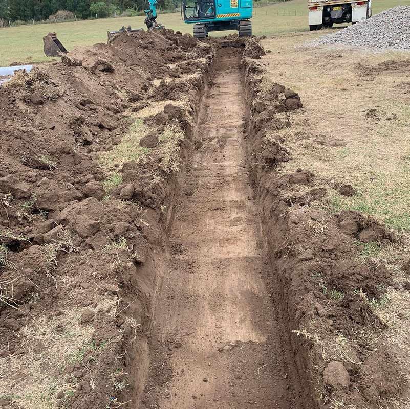 A Blue Kobelco Excavator Is Digging A Trench — Atholyn Earthmovers in Gosford, NSW