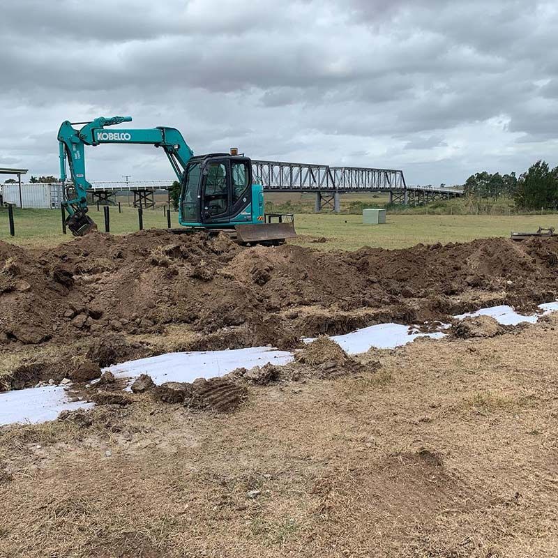 A Blue Kobelco Excavator Is Digging A Hole With Bridge In The Background — Atholyn Earthmovers in Wyong, NSW