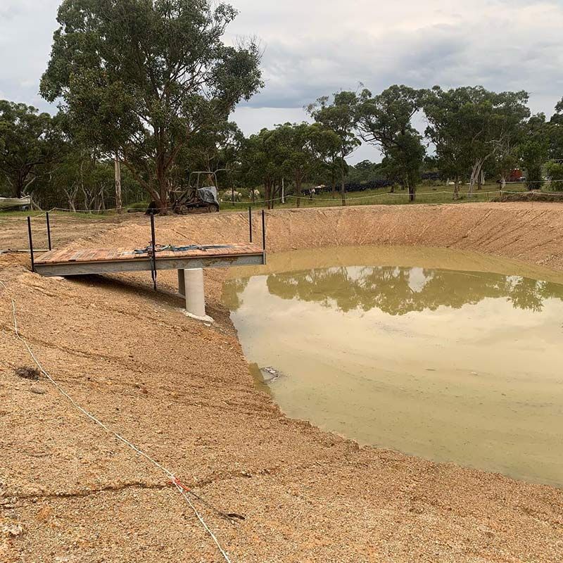 A Large Hole With Water Is Surrounded By Gravel And Trees — Atholyn Earthmovers in Gosford, NSW