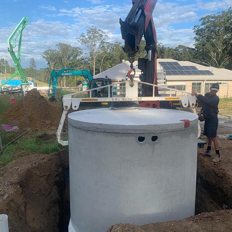 A Man Is Standing Next To A Large Concrete Cylinder Being Lifted By A Crane — Atholyn Earthmovers in Branxton, NSW