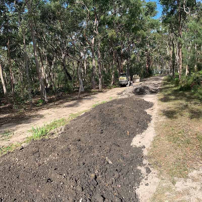 A Dirt Road In The Middle Of A Forest With Trees On Both Sides With Excavator — Atholyn Earthmovers in Branxton, NSW