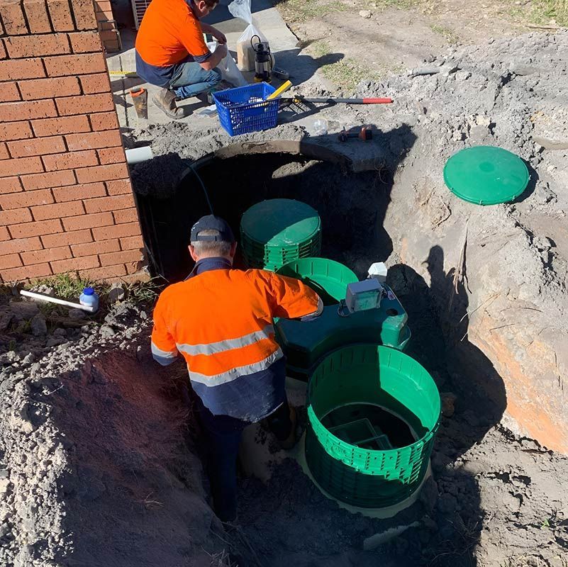 A Man In An Orange Shirt Is Working In A Hole With Green Septic Tank — Atholyn Earthmovers in Gosford, NSW