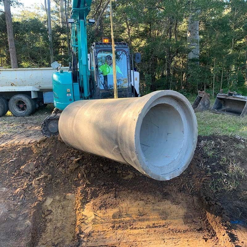A Large Concrete Pipe Is Being Lifted By A Bulldozer — Atholyn Earthmovers in Branxton, NSW