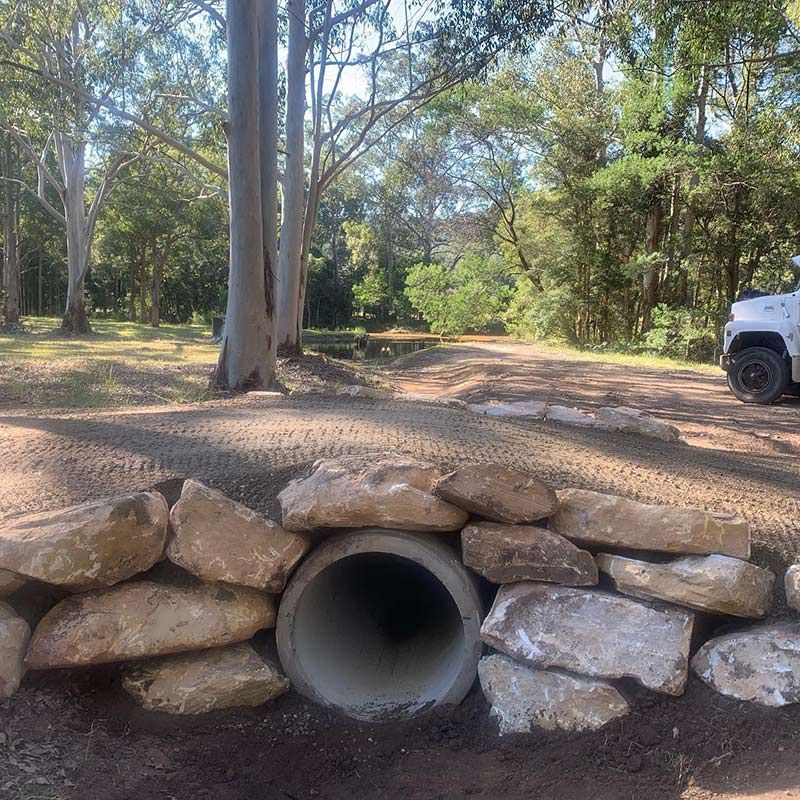 A White Truck Is Parked On The Side Of The Road Next To A Pipe Surrounded By Rocks — Atholyn Earthmovers in Wyong, NSW