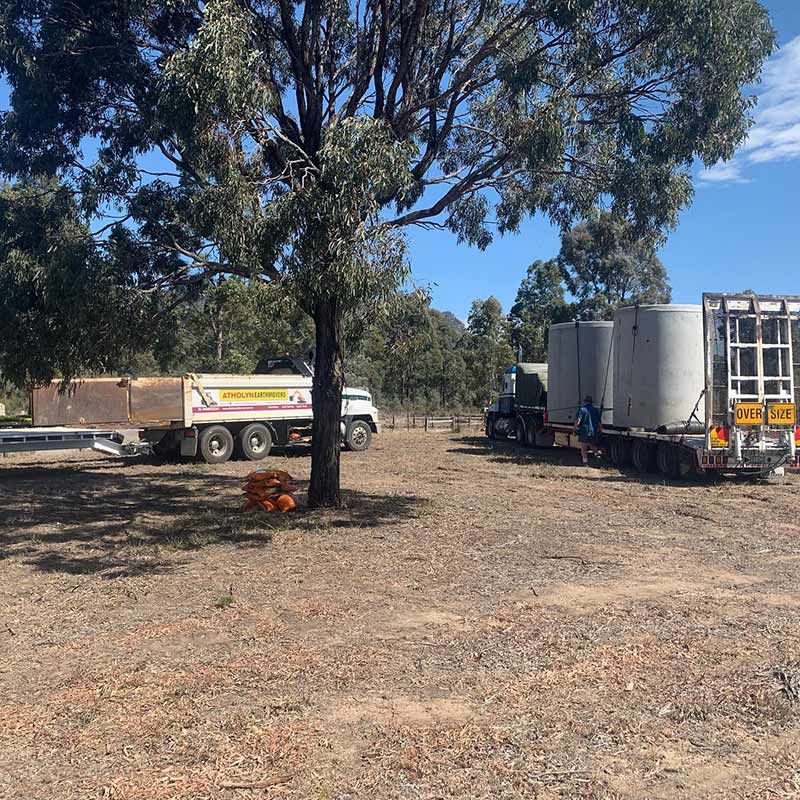 A Truck Is Parked In A Dirt Field Next To A Tree With Loaded Of Concrete Septic Tank — Atholyn Earthmovers in Singleton, NSW