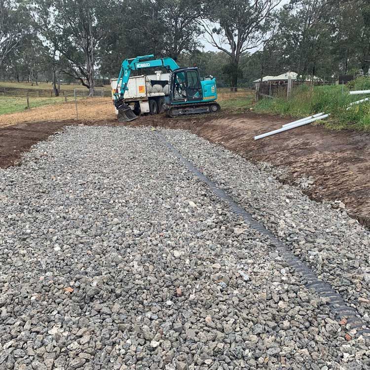 A Construction Vehicle And Excavator Is Driving Down A Gravel Road — Atholyn Earthmovers in Singleton, NSW