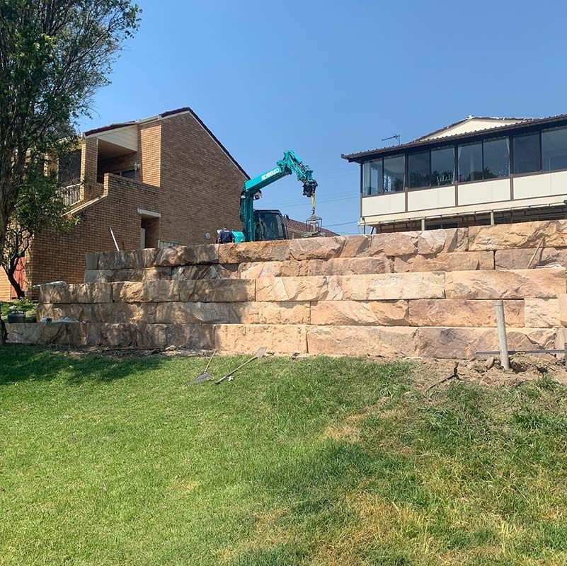 A Large Stone Wall Is Being Built In Front Of A House With Kobelco Excavator — Atholyn Earthmovers in Singleton, NSW